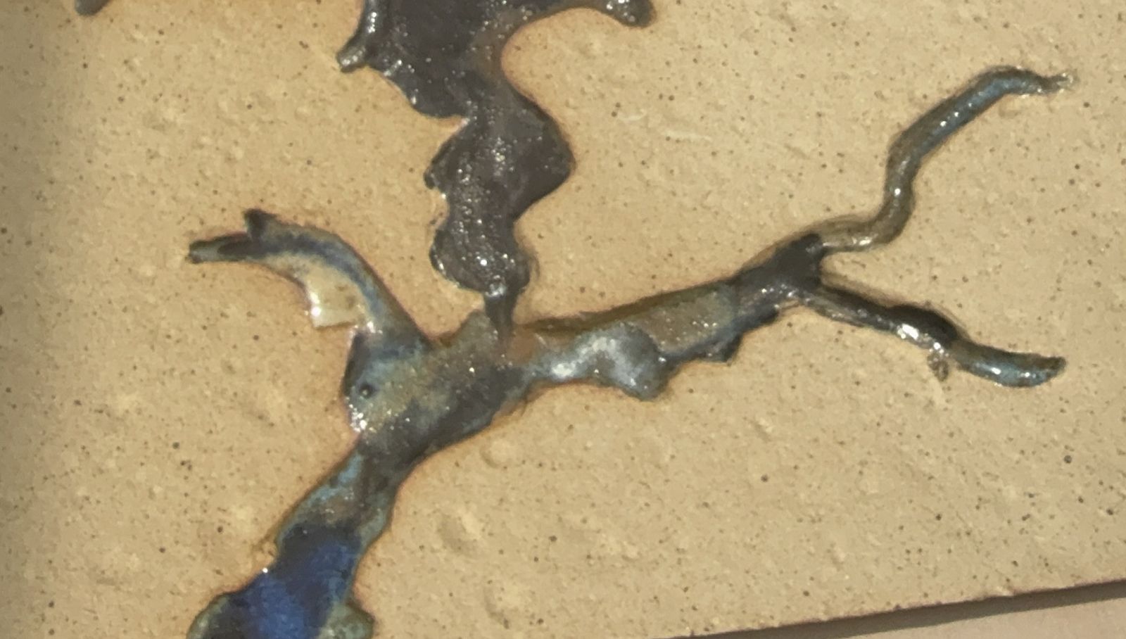 Glossy navy and blue glaze flowing across speckled sand-coloured stoneware